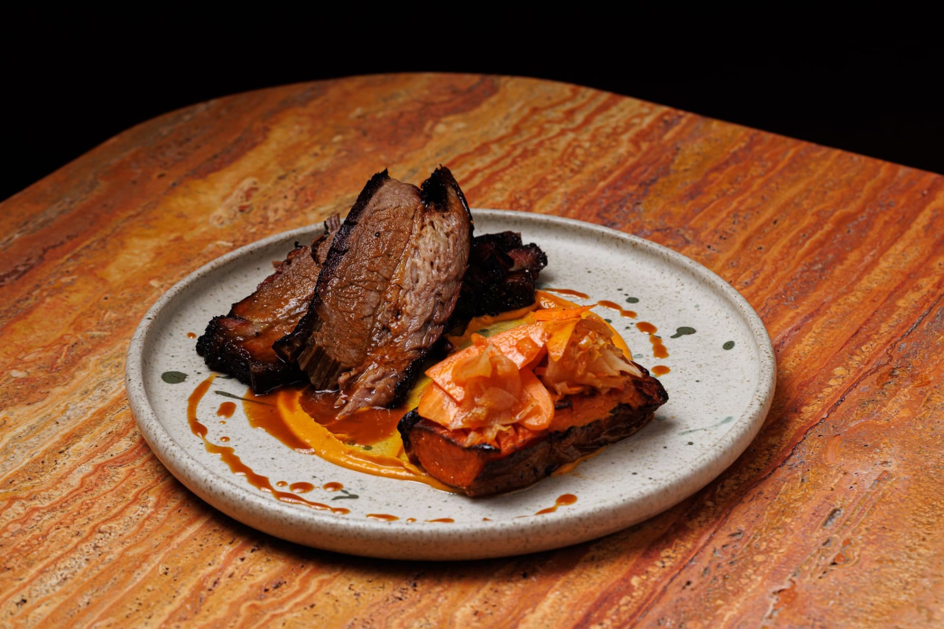Sliced brisket with roast carrot and kimchi on a stone table