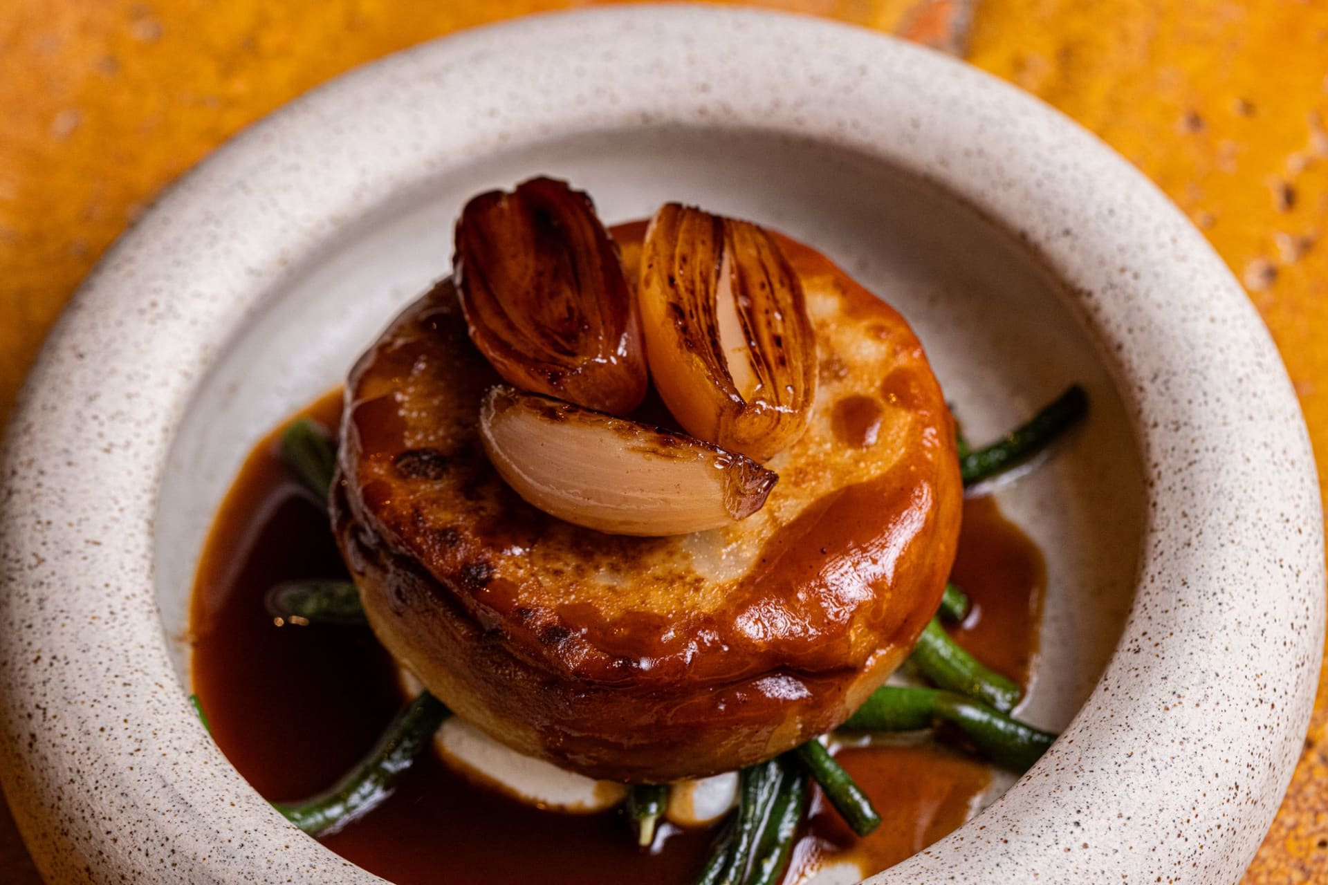 A glazed pie topped with charred shallots in a shallow bowl