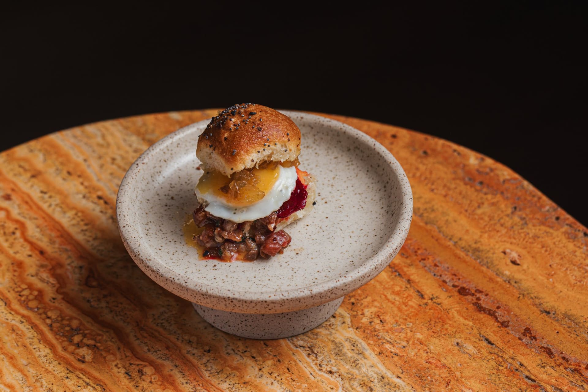 A brioche slider with fried egg on a raised stone plate
