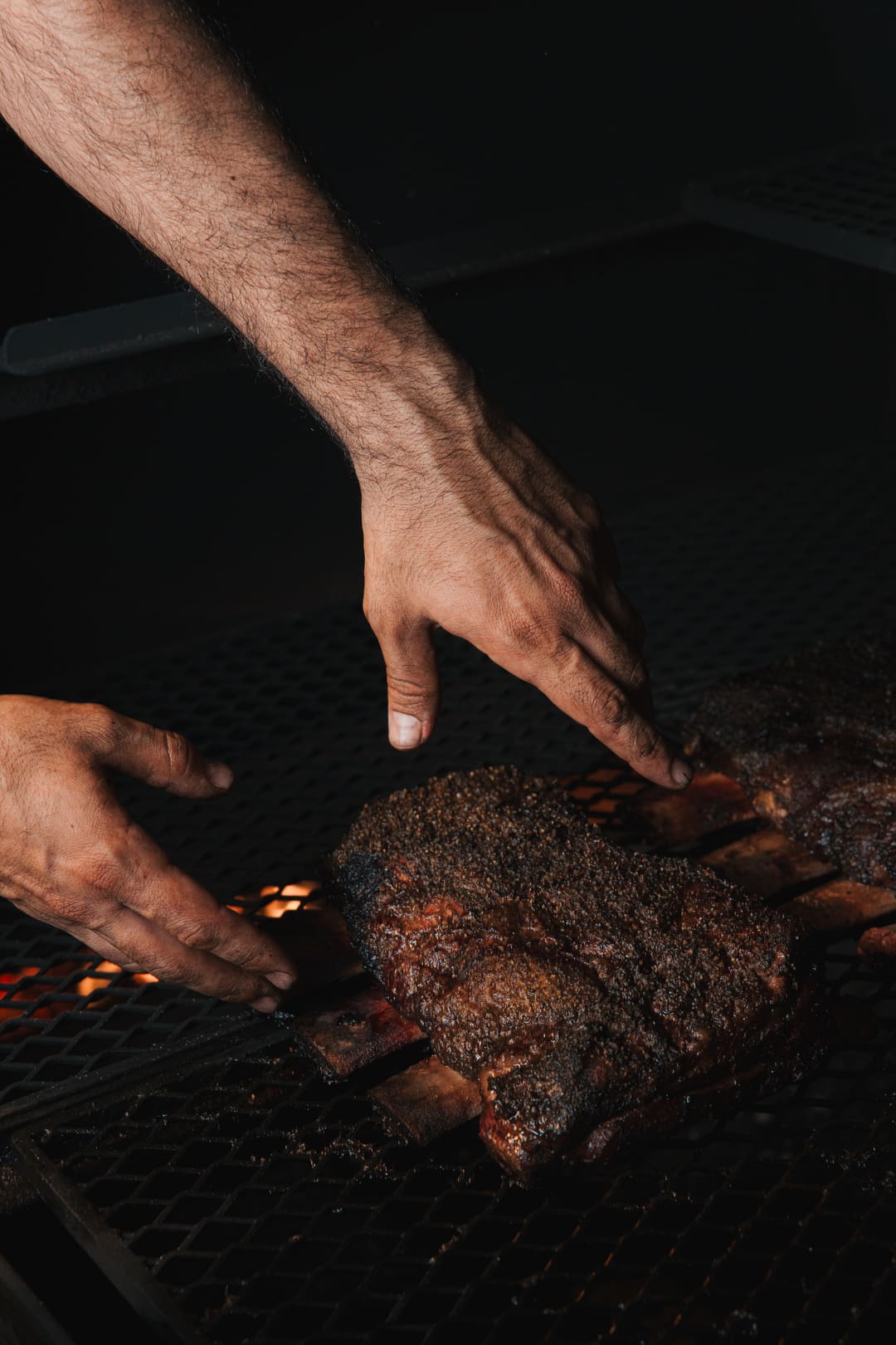 Hands lifting a brisket from the smoker