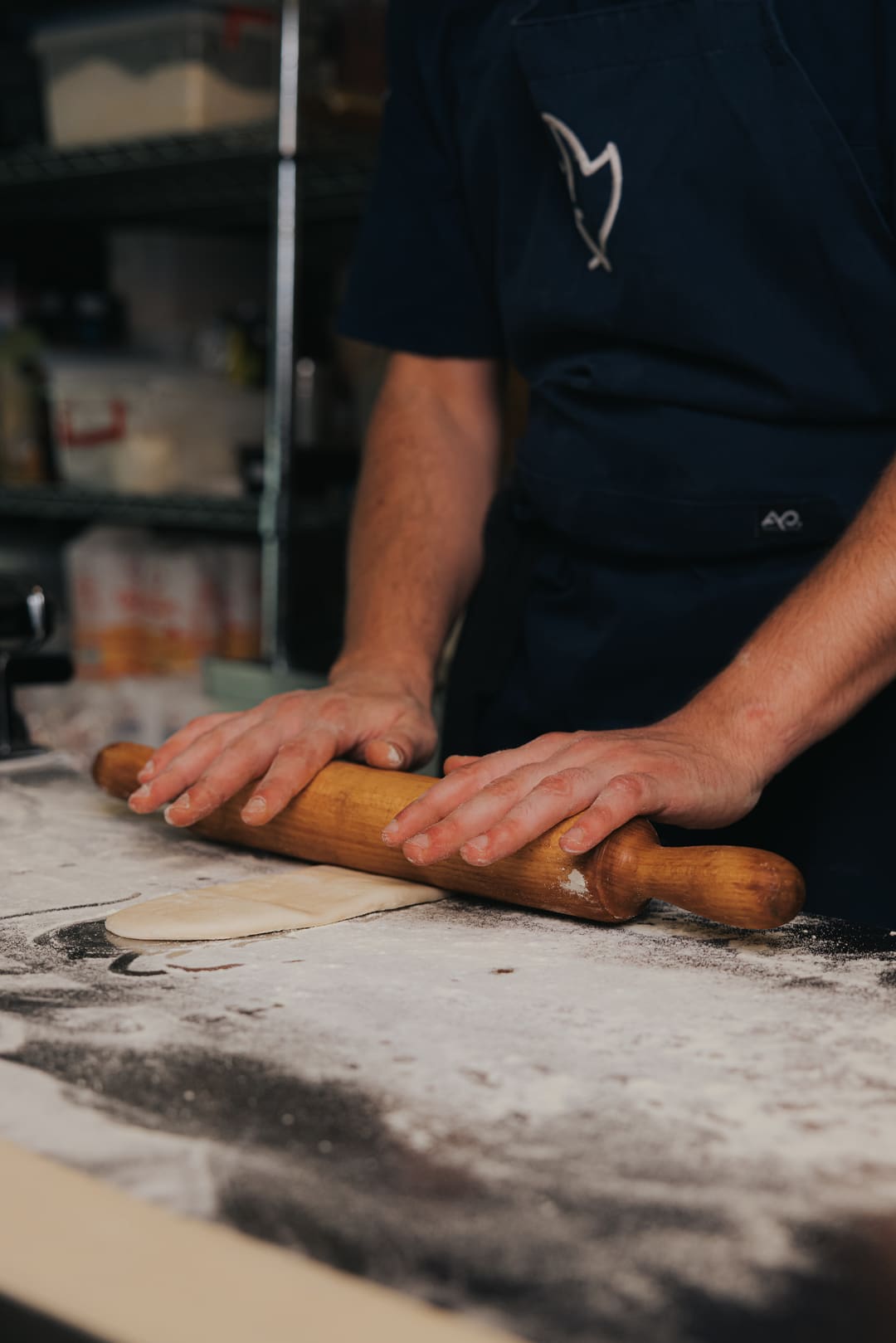 A cook rolling dough out on a floured bench